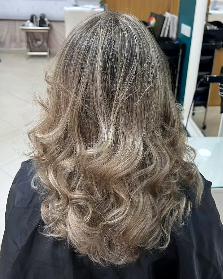 Balayage blond et brushing ondulé, devant le mur bleu pétrole